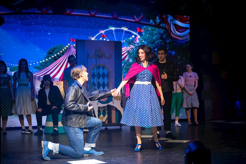 head of school shaking hands with a smiling graduate in cap and gown on stage